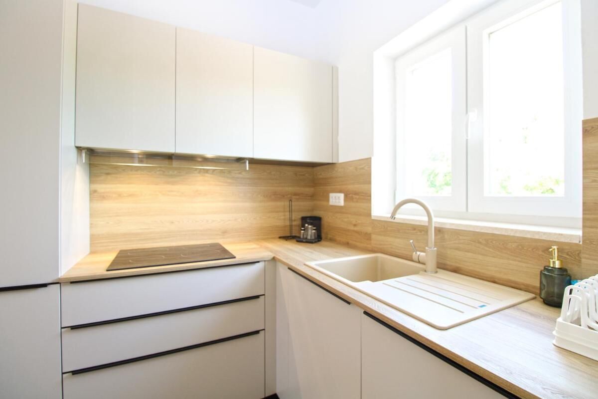 A modern kitchen with white cabinets, a wooden backsplash, a built-in sink, and a window providing natural light.