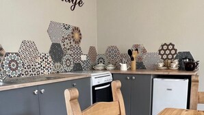 A kitchen with a wooden table and chairs, grey cabinets, and a wall decorated with vintage-style tiles.