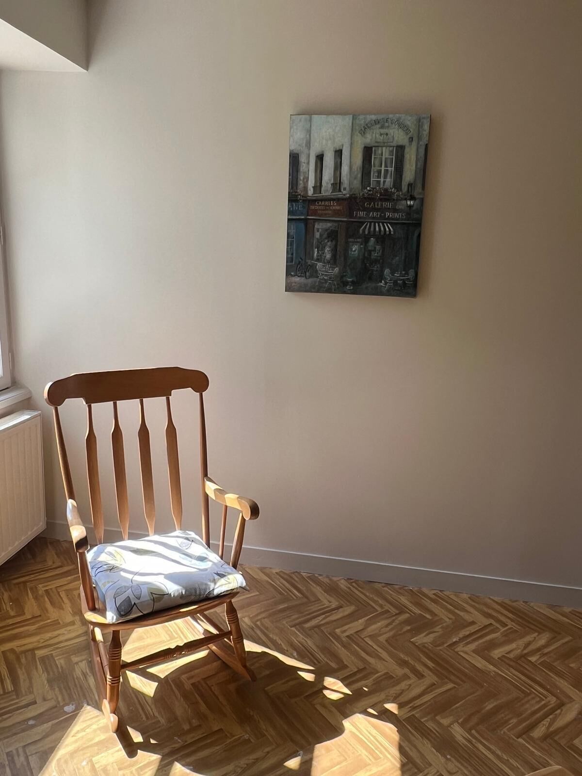 A wooden chair with a cushion in a room with wooden flooring and a wall-mounted painting.