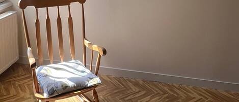 A wooden chair with a cushion in a room with wooden flooring and a wall-mounted painting.