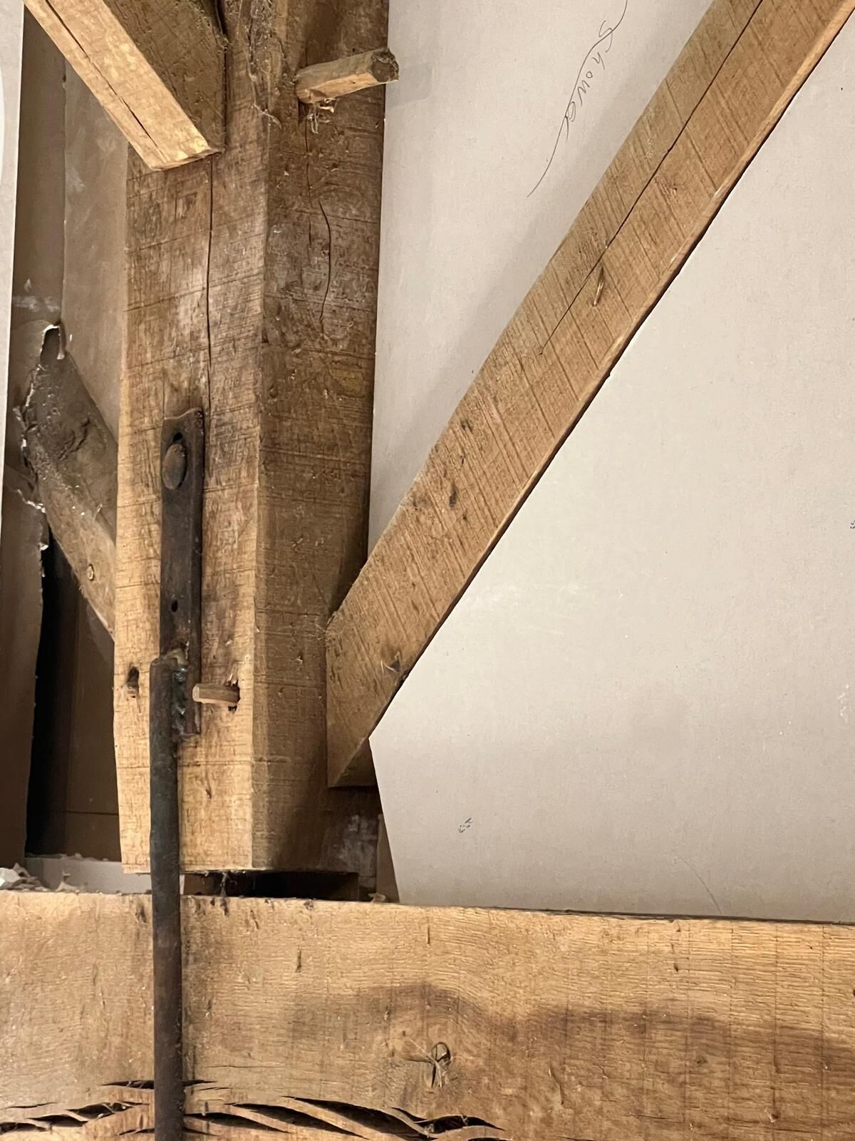 Een houten balkenconstructie met een metalen beugel en een wit paneel.