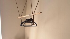 A corner of a room with a wooden chair, a wall-mounted rack with hangers, and a tiled floor.