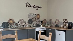 A kitchen with a wooden dining table and chairs, a white refrigerator, and a wall with a 'Vintage' sign.