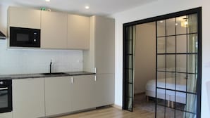 A modern kitchen with white cabinets, a black microwave, and a built-in oven. - Charming apartment near the sea (Cavalaire-sur-Mer)