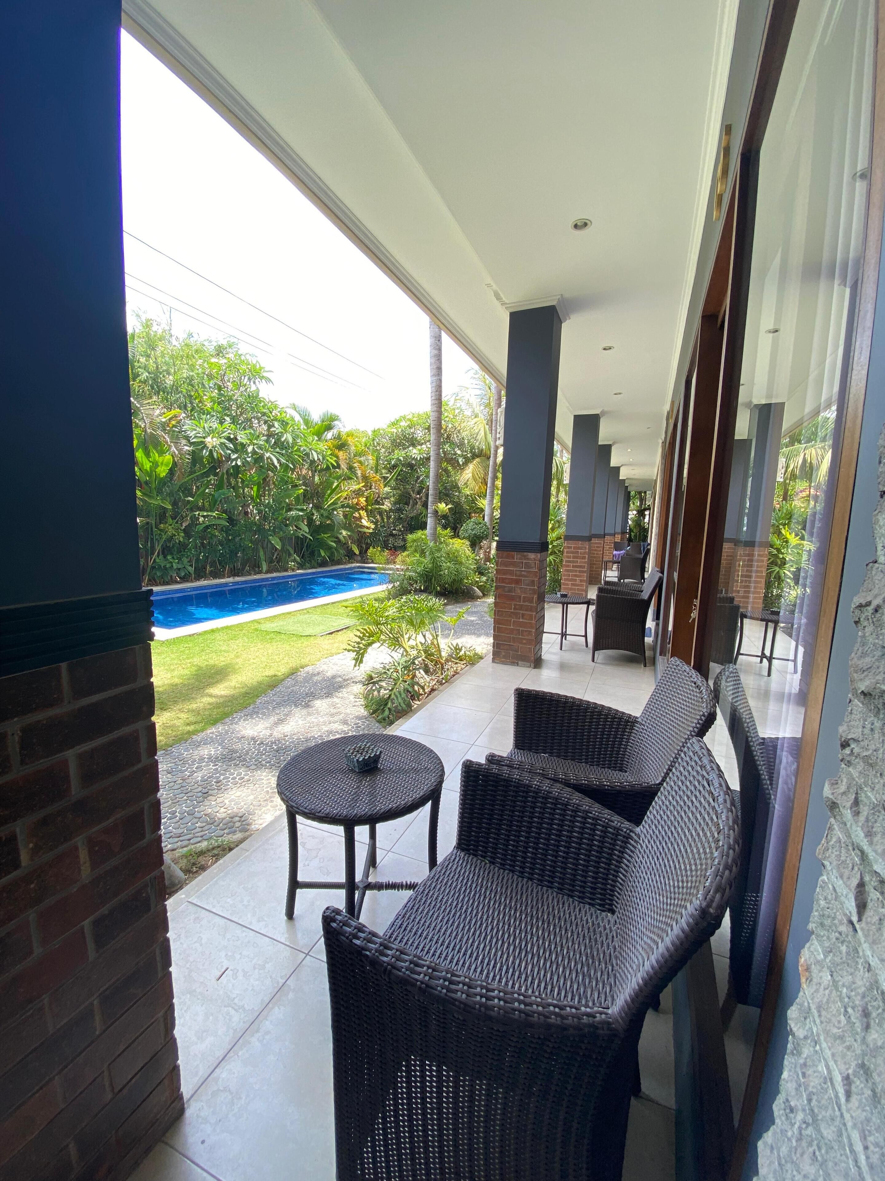 A covered outdoor area with wicker furniture, a pool, and a view of the surrounding greenery.