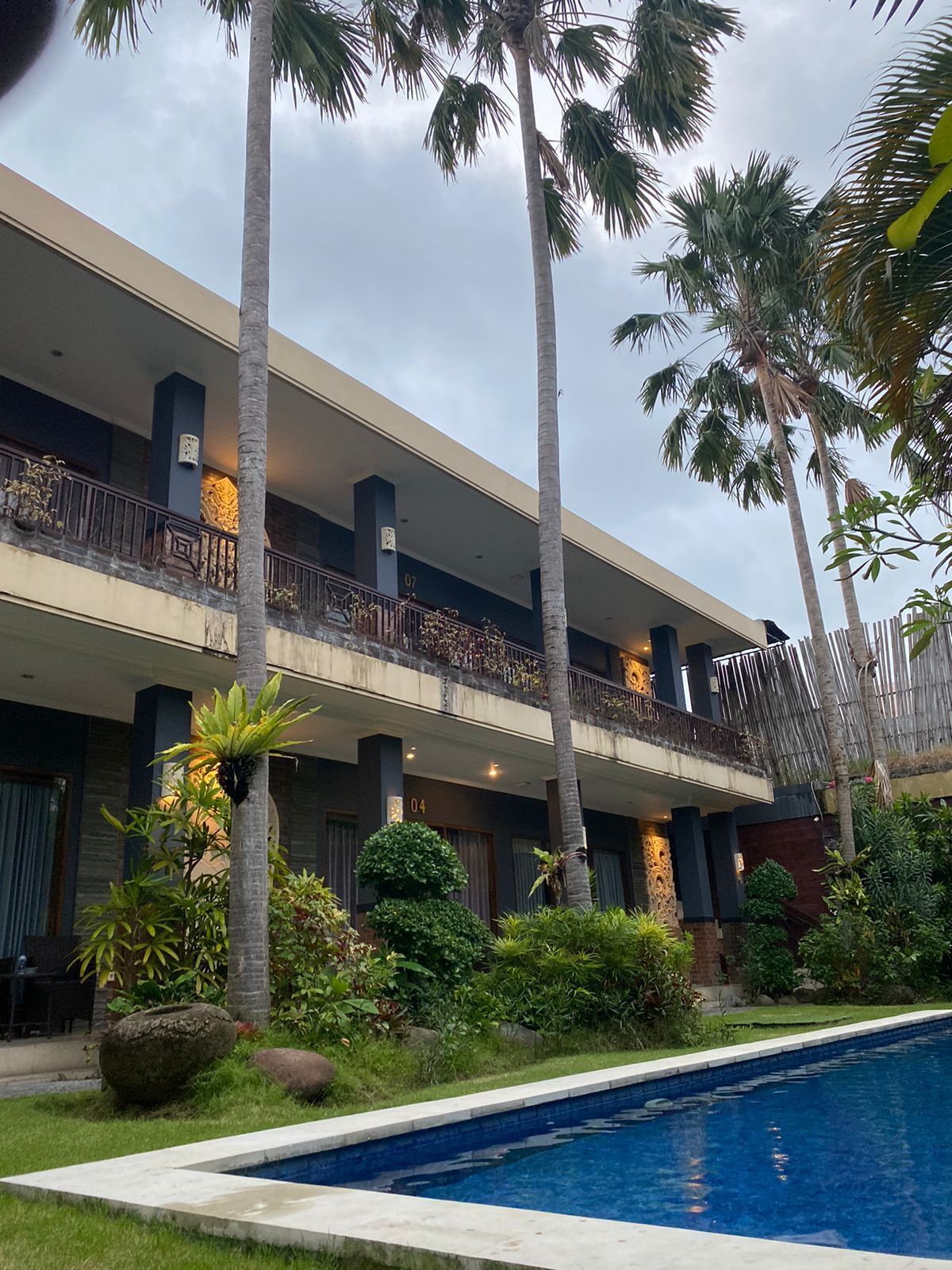 A hotel with a pool, palm trees, and a balcony with a railing.