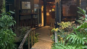 A rustic wooden structure with a tiled roof, a stone pathway leading to a wooden bench, and a bar area with shelves of bottles and framed pictures. - The Belong Canggu Bali By. SDM (Canggu)