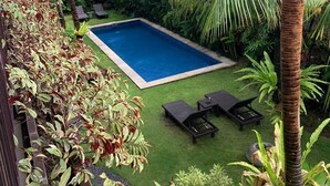 A swimming pool surrounded by lush greenery and palm trees, with lounge chairs and a small garden area. - The Belong Canggu Bali By. SDM (Canggu)