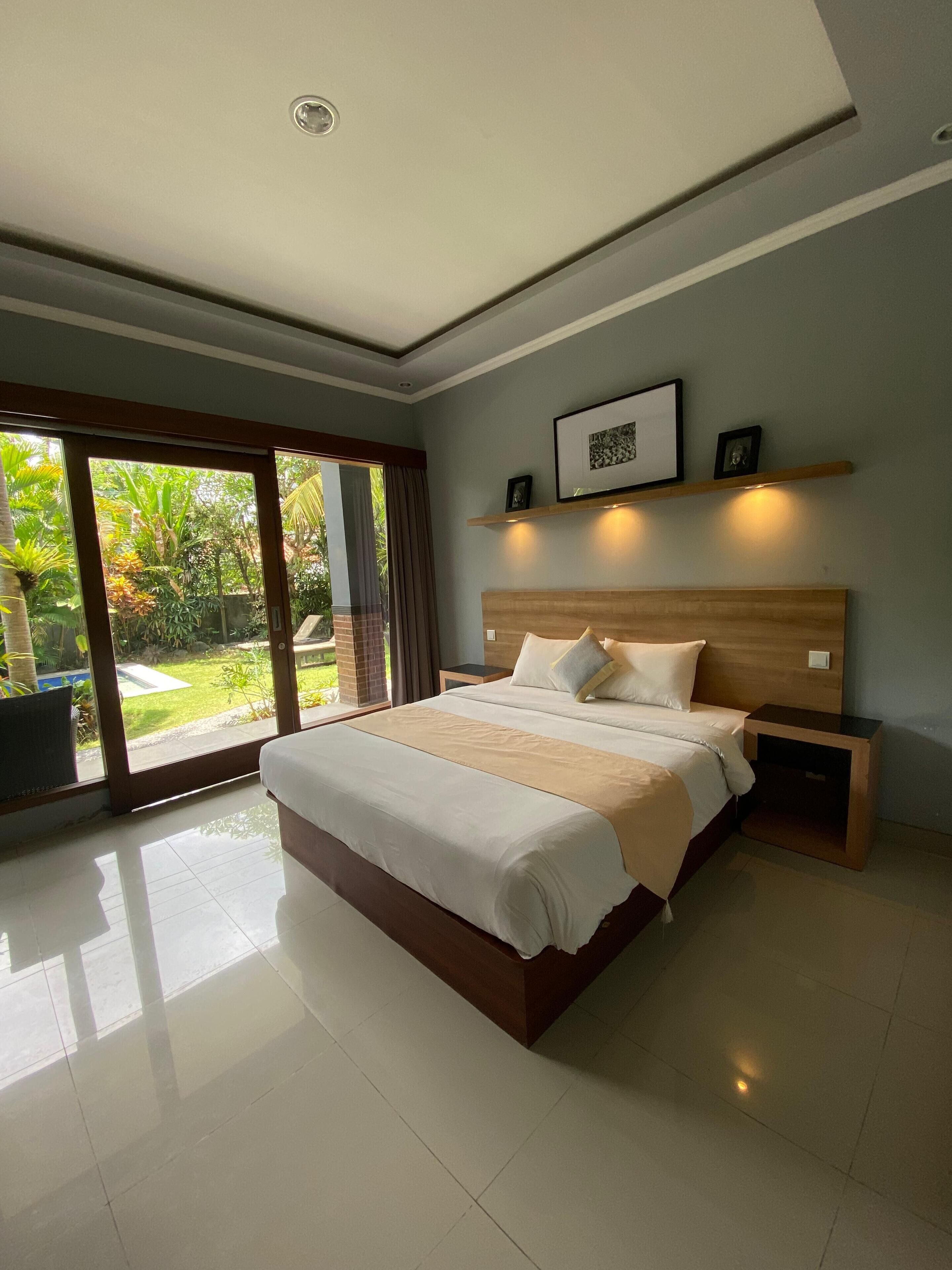 A modern bedroom with a large bed, a wooden headboard, a bedside table, and a picture frame on the wall.