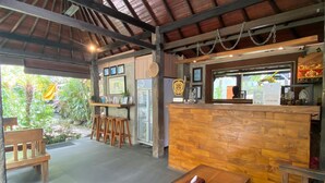 An indoor seating area with wooden tables and benches, a counter with a menu, and a ceiling with exposed beams. - The Belong Canggu Bali By. SDM (Canggu)