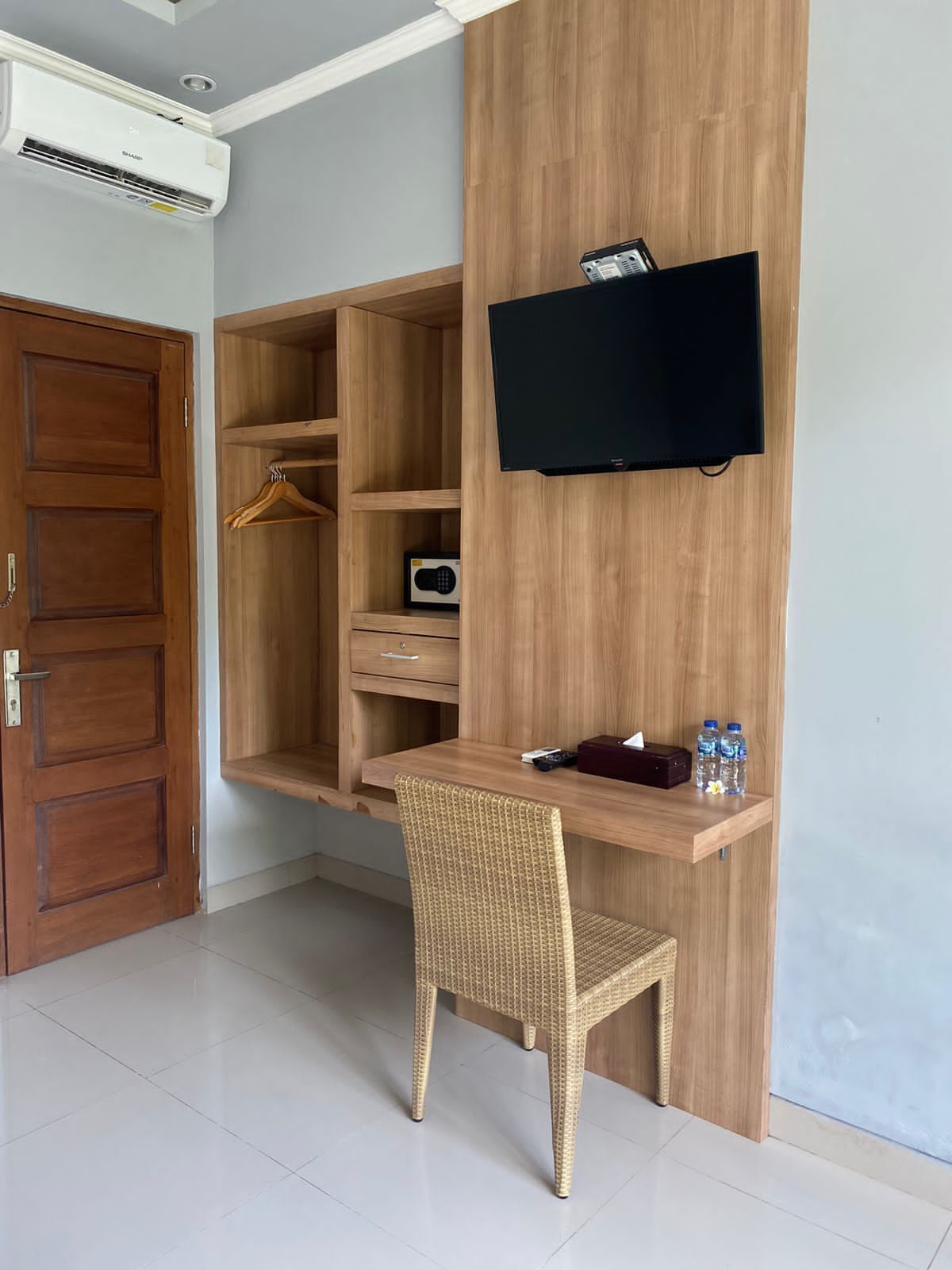Una camera compatta con una scrivania in legno, una sedia in vimini, una TV a muro e un armadio con una radio.