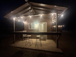 A covered outdoor area with a bar and two stools, a glass door, and a ceiling fan. - Charming studio with AC and WiFi in lovely Golden Shores (Golden Shores)