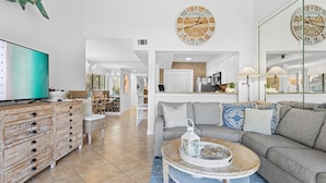 A modern living room with a television, a sofa, a coffee table, and a dining area in the background. - PlayaBella-Sandestin Escape|Lakefront|Golf Cart (Sandestin)