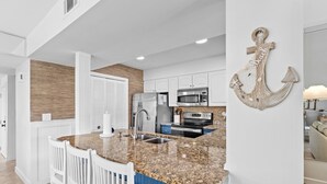 A modern kitchen with granite countertops, white cabinetry, and a large island with bar stools. - PlayaBella-Sandestin Escape|Lakefront|Golf Cart (Sandestin)