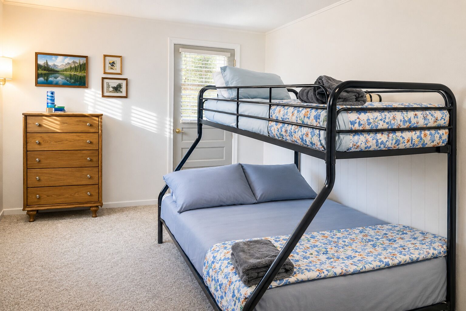 Un lit superposé avec un lit inférieur, une commode en bois et une porte avec des stores.