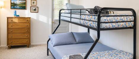 A bunk bed with a lower bunk, a wooden dresser, and a door with blinds.