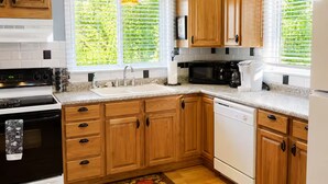 A modern kitchen with wooden cabinets, a black stove, a microwave, and a dishwasher. - Cranmore Retreat, Walk to Slopes, Hot Tub, Game Room, Dog-Friendly, Sleeps 16+ (Conway)