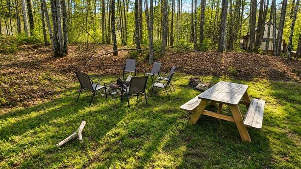 An outdoor seating area with a picnic table and chairs, surrounded by a forest. - Cranmore Retreat, Walk to Slopes, Hot Tub, Game Room, Dog-Friendly, Sleeps 16+ (Conway)