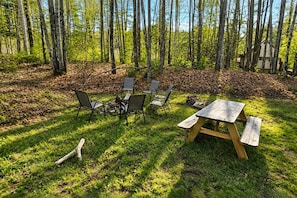 An outdoor seating area with a picnic table and chairs, surrounded by a forest. - Cranmore Retreat, Walk to Slopes, Hot Tub, Game Room, Dog-Friendly, Sleeps 16+ (Conway)