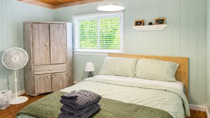 A bedroom with a bed, a wardrobe, a standing fan, a window with blinds, and a shelf with pictures. - Cranmore Retreat, Walk to Slopes, Hot Tub, Game Room, Dog-Friendly, Sleeps 16+ (Conway)