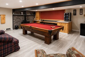 Une table de billard dans une pièce comprenant un coin cuisine, un canapé et un fauteuil à motifs.