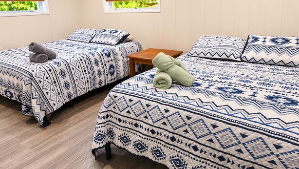A room with two beds, each with patterned bedding, a small wooden table, and a window with blinds. - Cranmore Retreat, Walk to Slopes, Hot Tub, Game Room, Dog-Friendly, Sleeps 16+ (Conway)