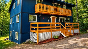A two-story blue house with a wooden balcony and a small porch. - Cranmore Retreat, Walk to Slopes, Hot Tub, Game Room, Dog-Friendly, Sleeps 16+ (Conway)