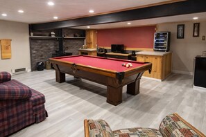 A pool table in a room with a red wall, a wooden cabinet, and a television.