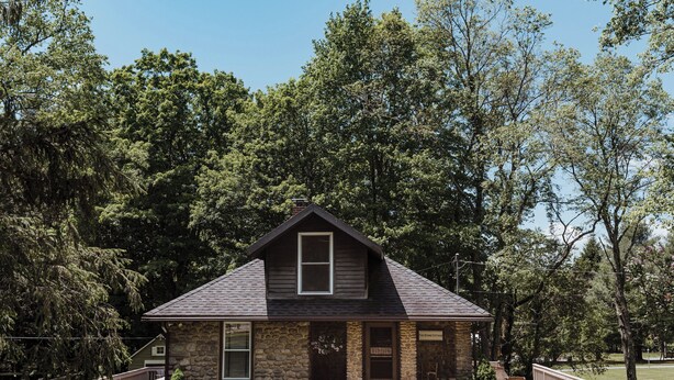 A stone house with a gabled roof, a front porch, and a small front yard.