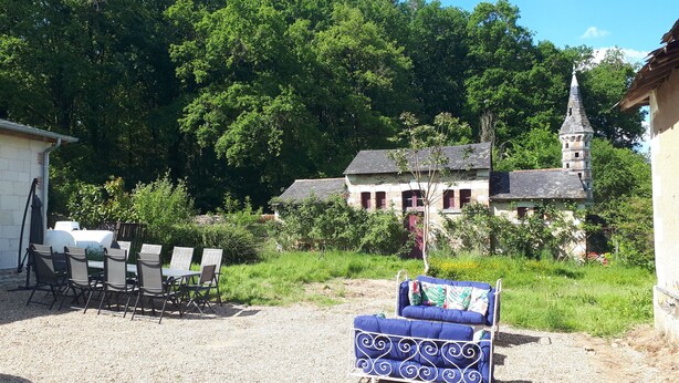 A gravel patio with outdoor seating, a rustic building with a tower, and lush greenery in the background. - Gîte du Château de Montriou - up to 12 people (Feneu)