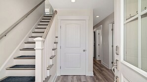A hallway with a wooden staircase, a white door, and a glass door on the right.