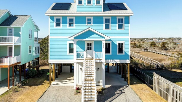A two-story house with solar panels on the roof, a front porch, and a staircase leading to the entrance.