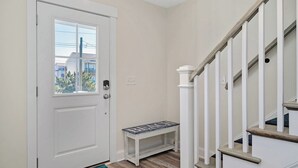 A hallway with a white door, a bench with the word "BEACH" on it, and a staircase with white railings.