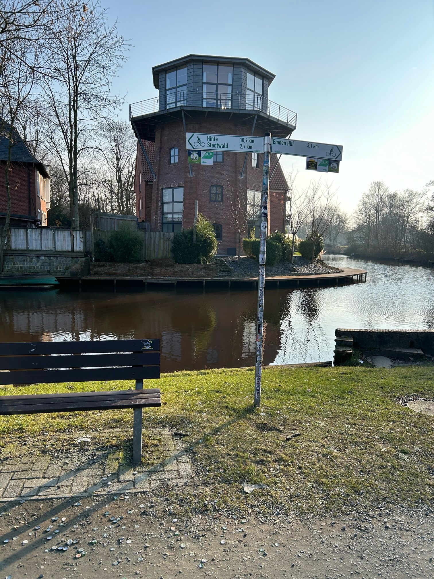 Una vista lungo il fiume, con una panchina, un edificio in mattoni e indicazioni stradali.