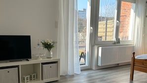 Moderni olohuone, jossa on televisio, kirjapinolla varustettu sohvapöytä, ikkuna, josta on näkymä rakennuksiin, ja patteri.