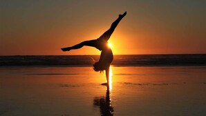 Une personne faisant la verticale sur une plage au coucher du soleil.
