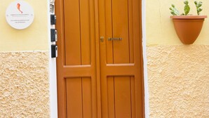 Une porte en bois à deux battants, surmontée d’une arche blanche, un panneau indiquant le numéro « 32 » sur le mur, et un pot de fleurs placé à droite.