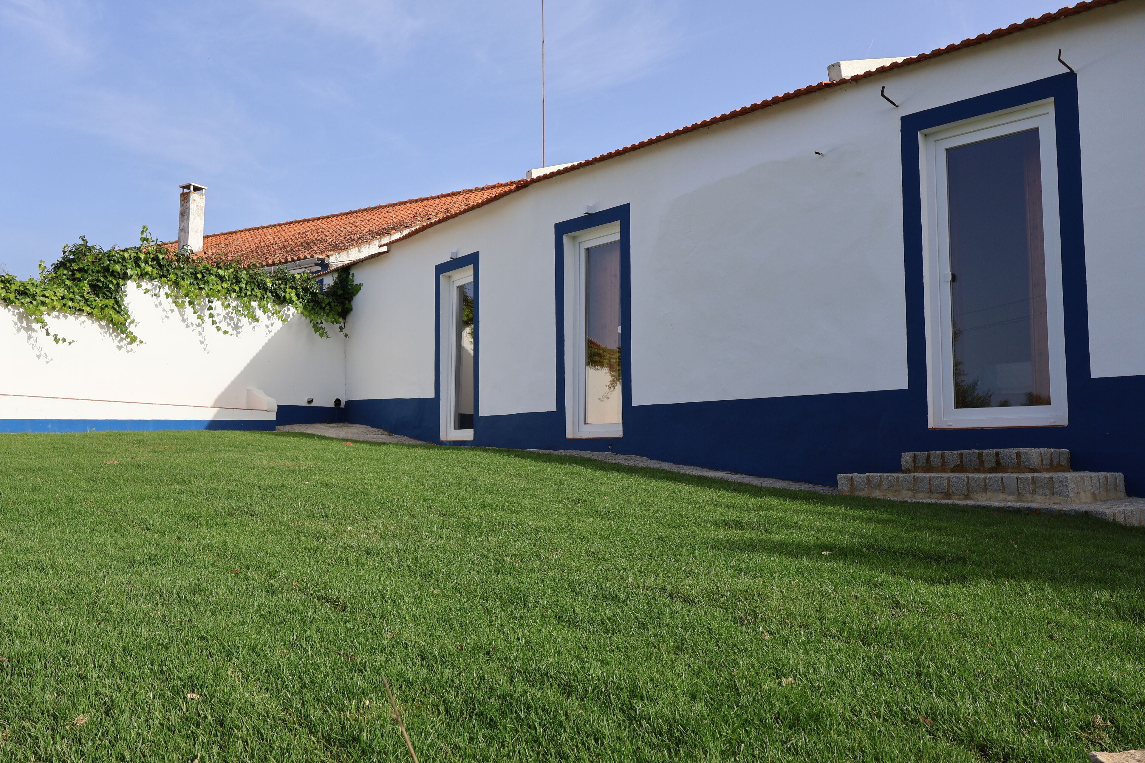 Ein Gebäude mit weißer Fassade und blauen Akzenten, das drei Türen und eine kleine Steintreppe zum Eingang zeigt.