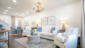 A spacious living room with a white sofa, a round coffee table, and a chandelier. There is a dining area with a table and chairs in the background. - The Magnolia, 3BR Luxe Stay by Velvet Ditch Villas (Oxford)