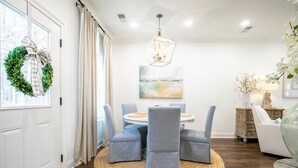 A dining area with a round table, four grey upholstered chairs, a woven rug, a chandelier, and a painting on the wall. - The Magnolia, 3BR Luxe Stay by Velvet Ditch Villas (Oxford)