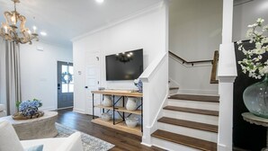 A modern living room with a wooden staircase, a flat-screen TV, and a decorative shelf with white pottery. - The Magnolia, 3BR Luxe Stay by Velvet Ditch Villas (Oxford)