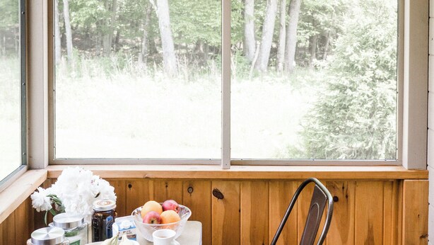 Una habitación acogedora con detalles de madera, una ventana con vistas a un bosque, una mesa con productos para el desayuno y dos sillas.