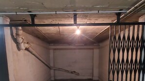 Ein leerer Raum mit Betonboden, einem Metallgitter und einer Decke mit freiliegenden Rohren.