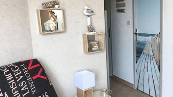Ein Zimmer mit einem Bett, einem Nachttisch mit Lampe, einer Wanduhr und einer Tür, die auf einen Balkon mit Meerblick führt.