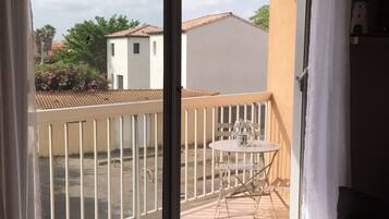 Ein Balkon mit Tisch und Stühlen, Blick auf benachbarte Gebäude und eine Tür zum Innenraum.