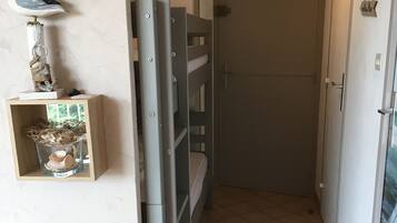 Ein schmaler Flur mit einem Etagenbett, einer kleinen Ablage mit Dekorationen und einer Tür mit einem Schild.