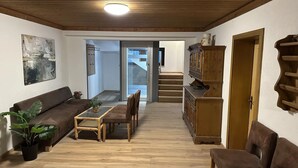 A living room with a wooden ceiling, a sofa, a dining table with chairs, a cabinet, and a staircase leading to another room. - Alpine Hideaway in Saalfelden (Saalfelden am Steinernen Meer)