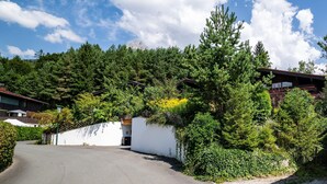 A modern building with a white exterior, surrounded by dense greenery and trees. - Alpine Hideaway in Saalfelden (Saalfelden am Steinernen Meer)