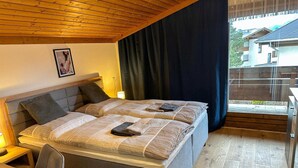 A double bed with a headboard, a bedside table, a chair, and a window with curtains. - Alpine Hideaway in Saalfelden (Saalfelden am Steinernen Meer)