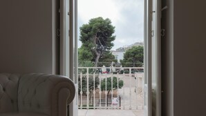 Une pièce avec vue sur un balcon accessible par une porte ouverte, agrémenté d’une balustrade blanche et d’un arbre.